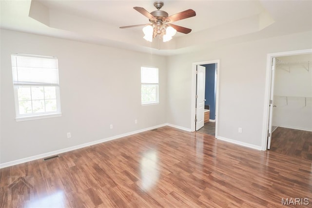 23332 Righteous Ln, Waynesville, MO 65583 - unfurnished bedroom with a tray ceiling, a walk in closet, multiple windows, and wood finished floors
