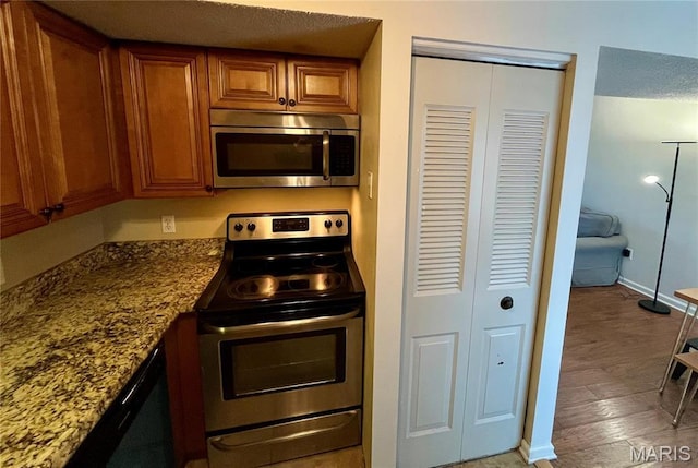 1504 Swallow Dr, Saint Louis, MO 63144 - kitchen with stainless steel appliances, brown cabinets, baseboards, dark stone counters, and light wood-type flooring