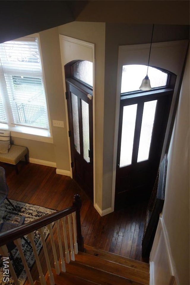 foyer entrance featuring dark wood-type flooring, baseboards, and stairway