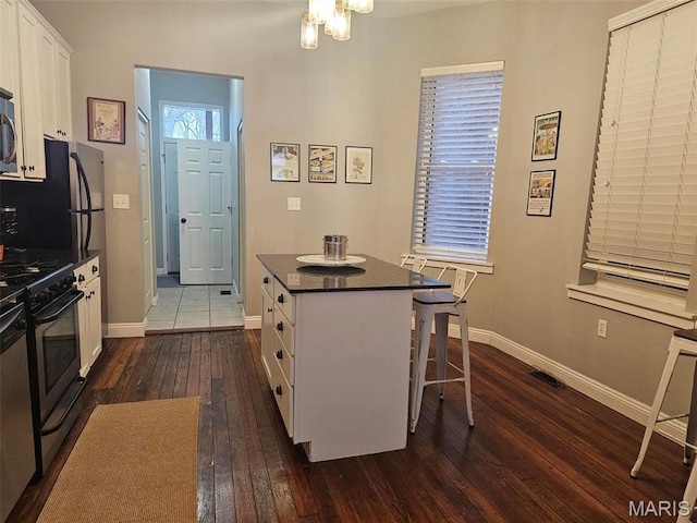 kitchen featuring appliances with stainless steel finishes, dark countertops, dark wood-style flooring, white cabinetry, and baseboards
