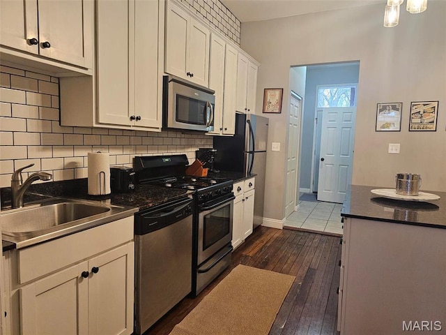 kitchen with appliances with stainless steel finishes, a sink, dark countertops, white cabinets, and tasteful backsplash