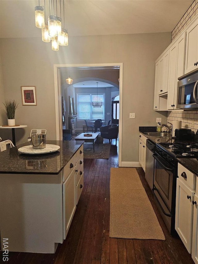 kitchen with stainless steel appliances, arched walkways, a sink, a chandelier, and white cabinetry