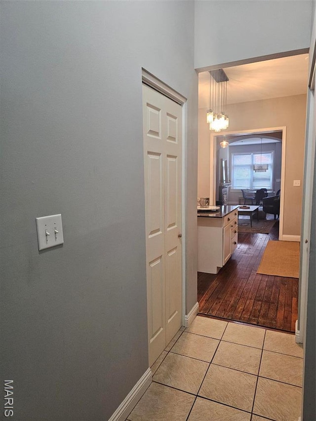 corridor with tile patterned flooring, baseboards, and a chandelier