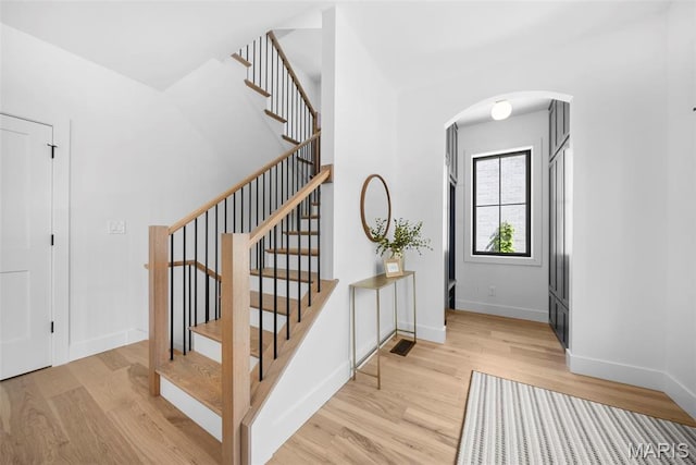 stairway with arched walkways, wood finished floors, and baseboards