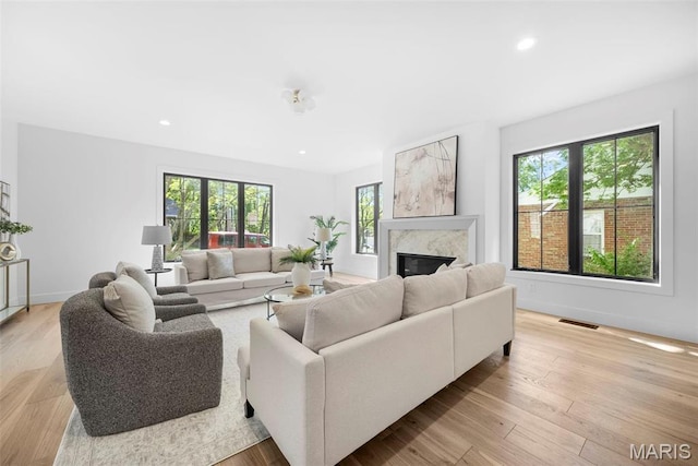 living room with a high end fireplace, recessed lighting, light wood-style flooring, and baseboards