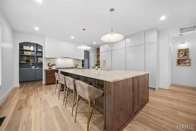 kitchen with light wood-style flooring, a large island with sink, a kitchen breakfast bar, light stone counters, and baseboards
