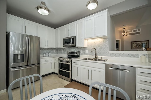 kitchen with stainless steel appliances, a sink, tasteful backsplash, light countertops, and white cabinetry