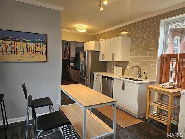 kitchen featuring a sink, appliances with stainless steel finishes, crown molding, dark wood-style flooring, and white cabinetry