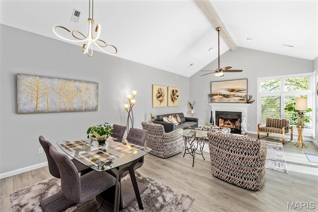 living area featuring beam ceiling, light wood-type flooring, a lit fireplace, ceiling fan, and baseboards