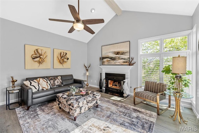 living area featuring wood finished floors, ceiling fan, a fireplace with flush hearth, beam ceiling, and baseboards