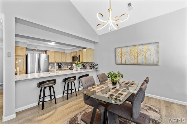 dining space featuring a chandelier, light wood finished floors, baseboards, and vaulted ceiling