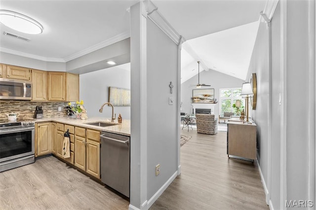 kitchen featuring appliances with stainless steel finishes, a sink, light wood-style floors, light brown cabinetry, and tasteful backsplash
