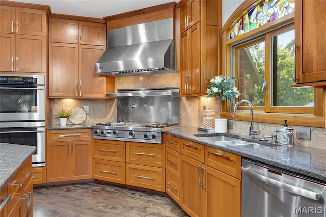 10711 Kennerly Rd, Saint Louis, MO 63128 - kitchen featuring stainless steel appliances, wall chimney range hood, a sink, brown cabinetry, and dark stone countertops