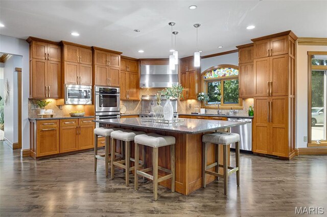 10711 Kennerly Rd, Saint Louis, MO 63128 - kitchen with wall chimney exhaust hood, stainless steel appliances, dark wood-style floors, a kitchen island, and brown cabinetry