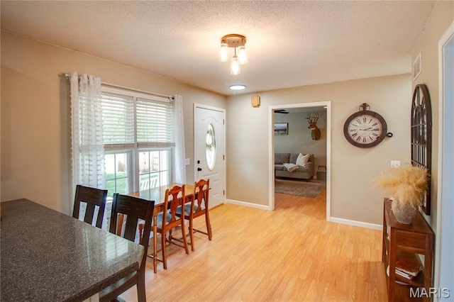 dining space with light wood-type flooring, baseboards, and a textured ceiling