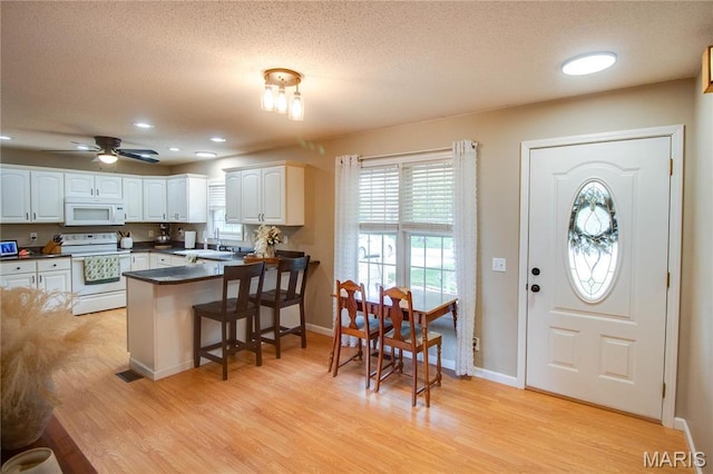 kitchen with white appliances, dark countertops, a peninsula, white cabinets, and light wood-type flooring