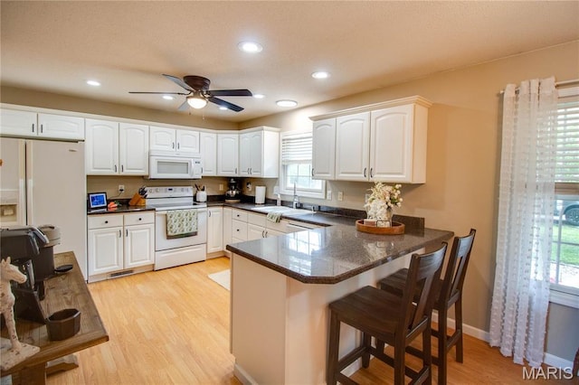 kitchen with white appliances, a sink, a peninsula, light wood-style floors, and white cabinetry