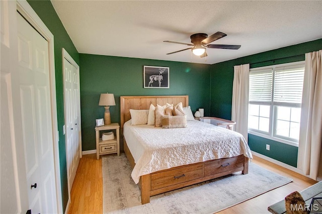 bedroom with light wood-type flooring, baseboards, a closet, and a ceiling fan