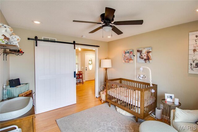 bedroom featuring wood finished floors, a barn door, a crib, recessed lighting, and a ceiling fan