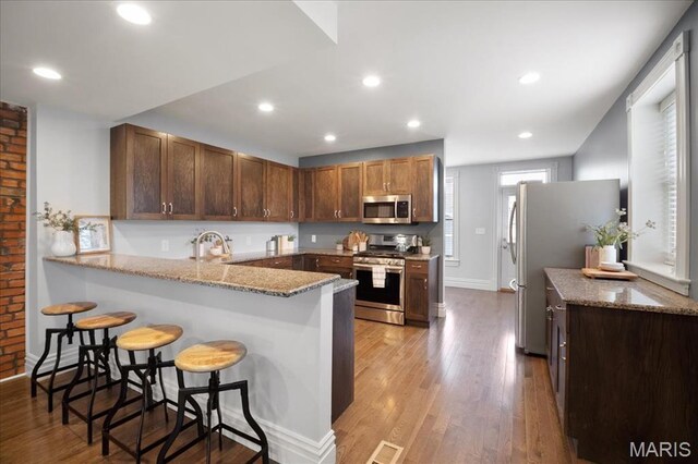 3974 Utah St, Saint Louis, MO 63116 - kitchen with appliances with stainless steel finishes, a peninsula, light stone counters, a breakfast bar area, and light wood-type flooring