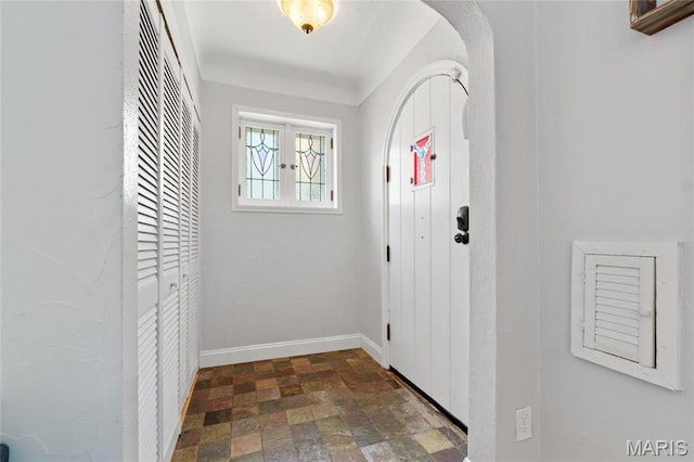 doorway to outside with stone finish flooring, arched walkways, and baseboards