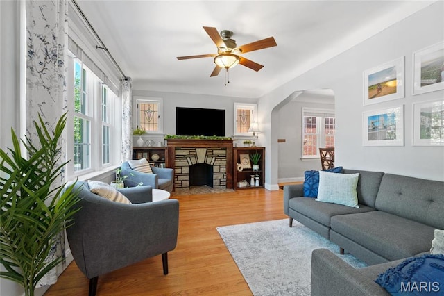 living area with arched walkways, a fireplace, light wood-style flooring, and plenty of natural light