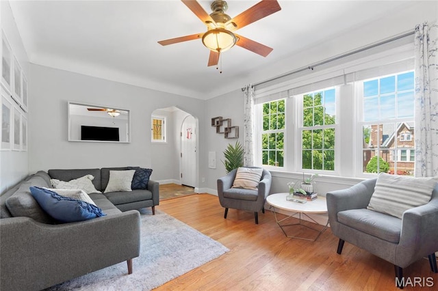 living area with ceiling fan, arched walkways, light wood-type flooring, and baseboards