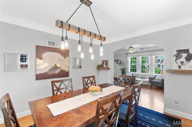dining room with arched walkways, wood finished floors, baseboards, and ceiling fan