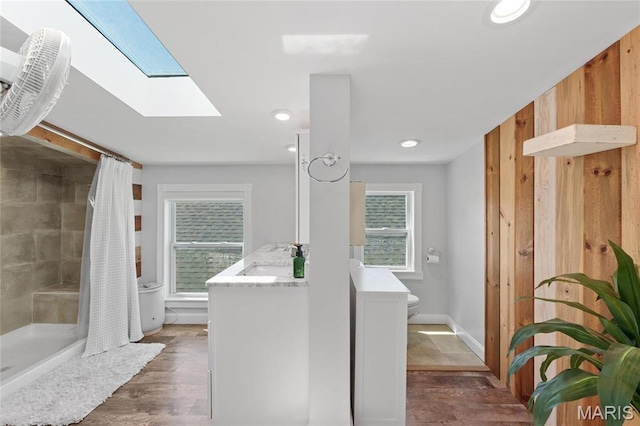 bathroom with a skylight, a shower stall, toilet, vanity, and wood finished floors