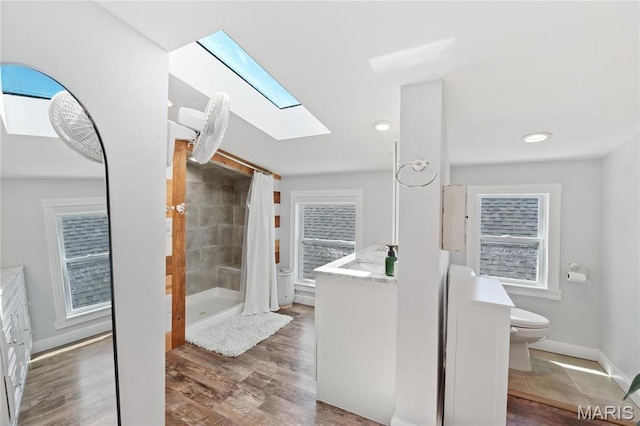 full bathroom featuring a skylight, a shower stall, toilet, vanity, and wood finished floors
