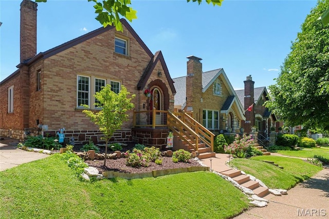 english style home with brick siding, a chimney, and a front lawn