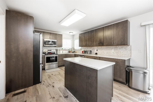 kitchen with stainless steel appliances, a sink, tasteful backsplash, and light wood-style floors