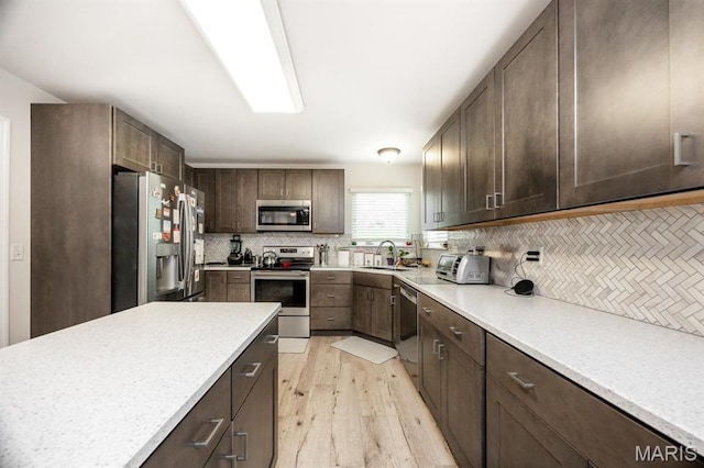 kitchen featuring stainless steel appliances, decorative backsplash, dark brown cabinetry, a sink, and light wood-style floors