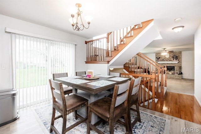 dining space featuring stairs, a chandelier, light wood-style floors, and a brick fireplace