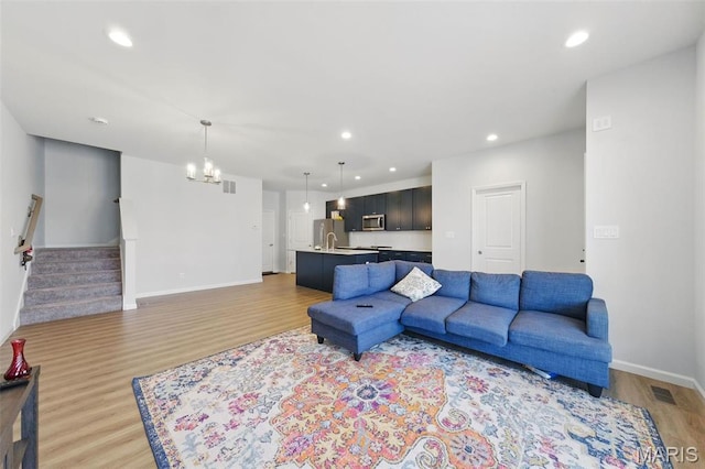living area with light wood-style floors, recessed lighting, baseboards, stairs, and a chandelier
