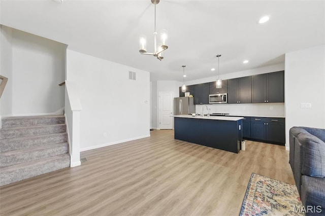 kitchen with stainless steel appliances, open floor plan, light countertops, light wood finished floors, and a chandelier