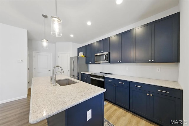 kitchen featuring stainless steel appliances, a sink, light wood finished floors, an island with sink, and blue cabinetry