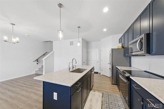 kitchen with appliances with stainless steel finishes, a sink, light wood-style flooring, a kitchen island with sink, and decorative light fixtures