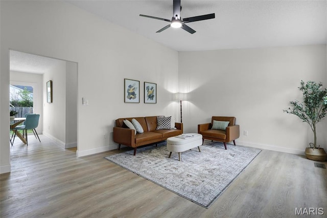 living area featuring light wood-style floors, baseboards, and a ceiling fan
