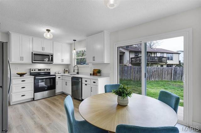 kitchen featuring stainless steel appliances, white cabinets, light countertops, light wood-style flooring, and a textured ceiling