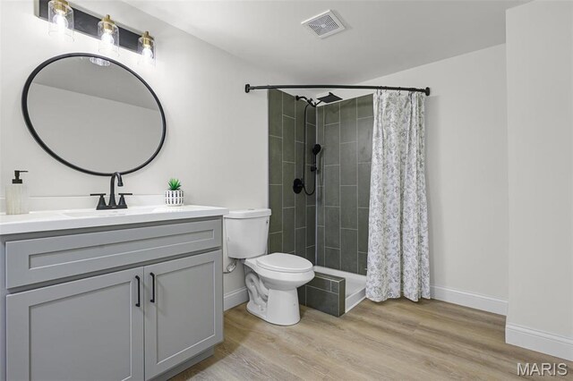 full bathroom featuring toilet, wood finished floors, vanity, and tiled shower