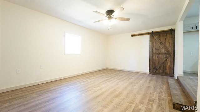 unfurnished bedroom with a barn door, wood finished floors, baseboards, and a ceiling fan