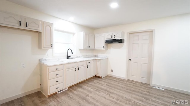 kitchen with a sink, under cabinet range hood, light wood-style flooring, light countertops, and recessed lighting