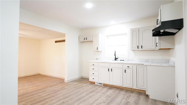 kitchen with a sink, light wood finished floors, light countertops, baseboards, and white cabinets