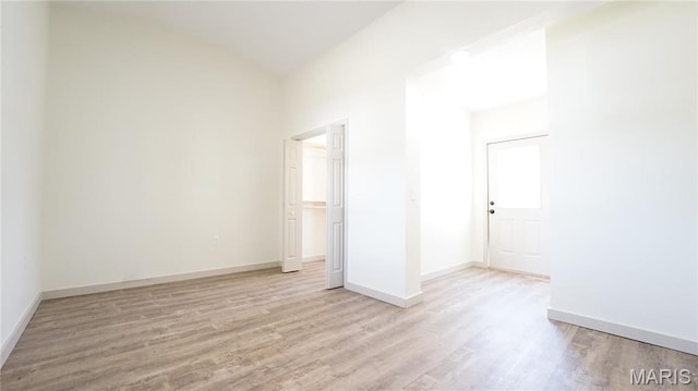empty room with light wood-type flooring, baseboards, and lofted ceiling