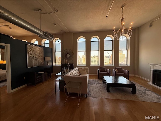 living area with wood finished floors, a fireplace, a chandelier, a textured ceiling, and baseboards