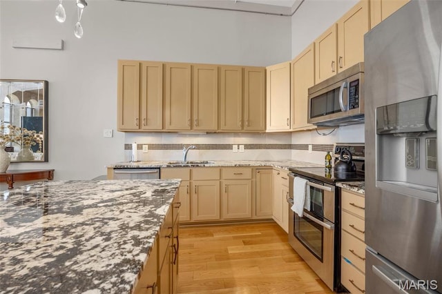 kitchen featuring stainless steel appliances, light brown cabinets, a sink, light wood-style flooring, and dark stone countertops