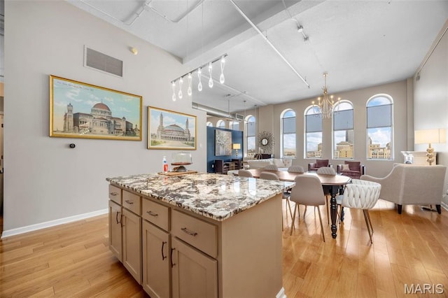 kitchen featuring open floor plan, light wood finished floors, a center island, light stone counters, and track lighting