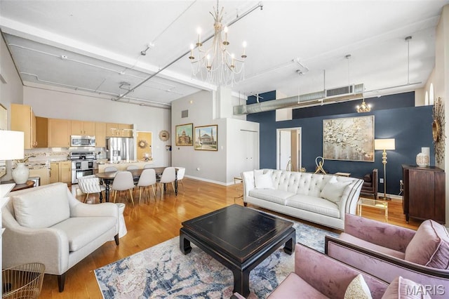 living area with a high ceiling, baseboards, light wood-style floors, a chandelier, and rail lighting