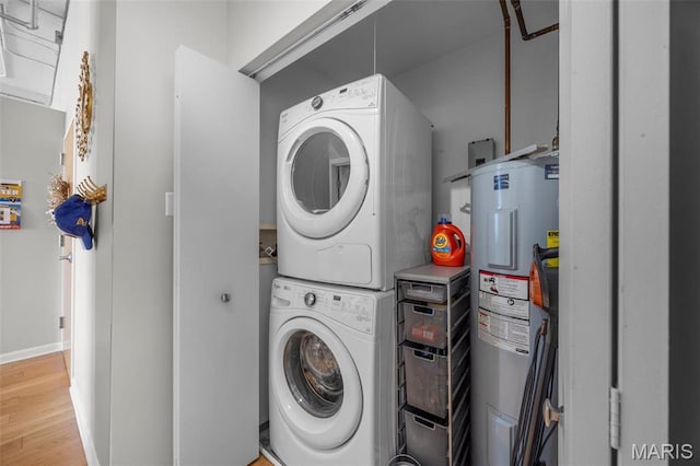 clothes washing area with stacked washer / dryer, electric water heater, light wood-type flooring, and baseboards